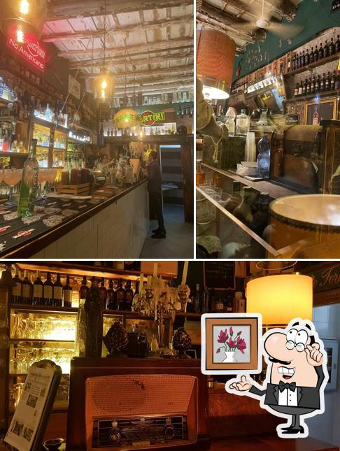 Il banco del bar visto per lungo, con le bottiglie, il soffitto di legno e l'insegna Martini accesa